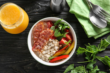 Bowl with delicious oatmeal, bacon, herbs and vegetables on wooden table