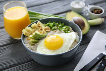 Bowl with delicious oatmeal, egg and avocado on wooden table