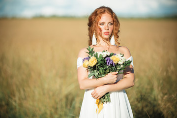 Naklejka na ściany i meble Portrait of pretty bride with freckles on her face in field with bridal bouquet of wildflowers