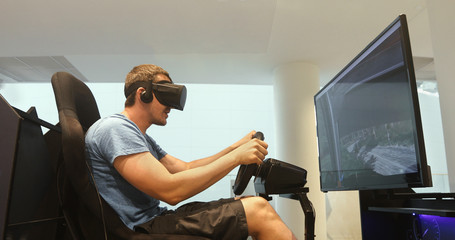 Side view of gamer sitting and playing racing simulator game in virtual reality headset 