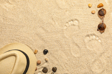 Fototapeta na wymiar Sunglasses, hat and footprints on beach sand