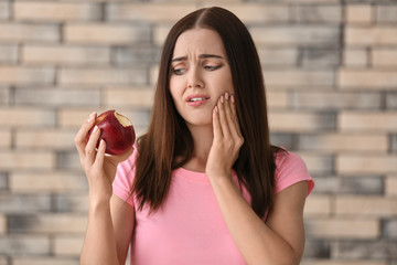 Young woman with sensitive teeth and apple on blurred background