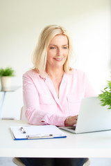 Beautiful elderly woman sitting in front of laptop and working from home. Home office.