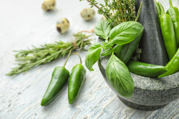 Mortar with fresh chili peppers and herbs on light background