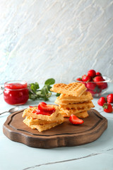 Board with waffles and strawberry jam on table