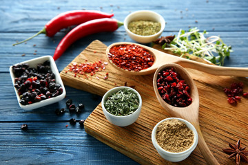 Bowls and spoons with different dry spices on wooden background
