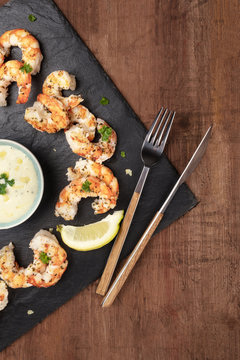 Overhead photo of plate of cooked shrimps on a dark rustic background, with a sauce, with a place for text