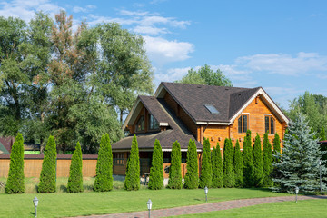Fototapeta na wymiar Beautiful luxury big wooden house. Timber cottage villa with with green lawn, garden and blue sky on background