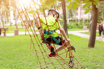 Little boy in safety equipment climbing on rope wall at adventure park. Children summer sport extreme outdoor activity. Back view