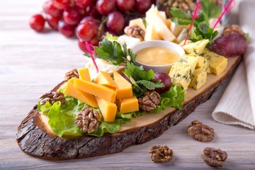 Cheese plate served with nuts and honey on wooden board. Tasty cold appetizer