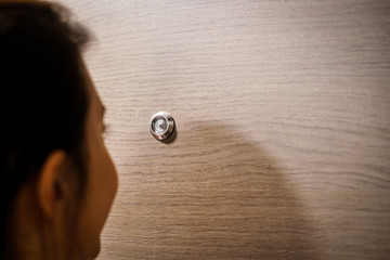 Naklejka premium young woman looking out through the peephole of her front door.