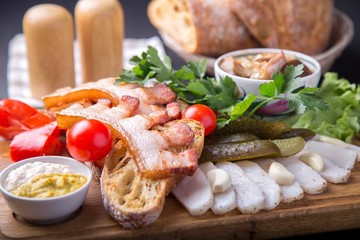 Snack with fried brisket, bread,  cut lard, fresh tomatoes and marinated mushrooms on wooden board. Cold snack