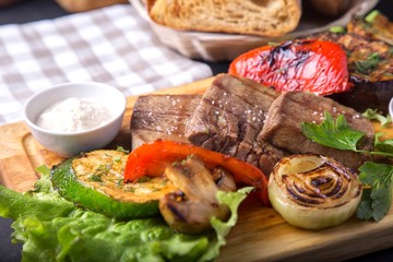 Grilled beef tongue served with vegetables and sauce on wooden board. Tasty beef tongue on a grill