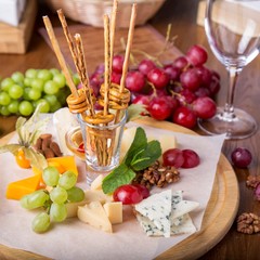 Cheese plates served with grapes, bread sticks and nuts on a wooden board.
