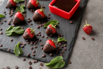 Slate plate with tasty chocolate dipped strawberries on grey table