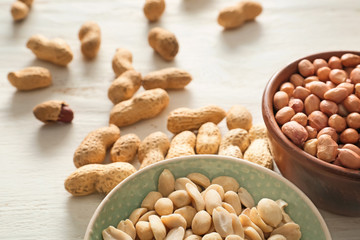 Bowls with tasty peanuts on white wooden background