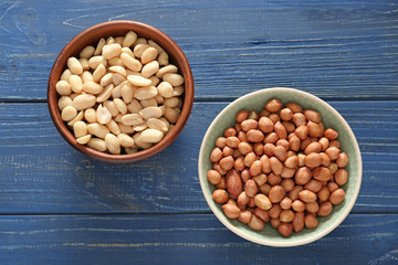 Bowls with tasty peanuts on wooden background