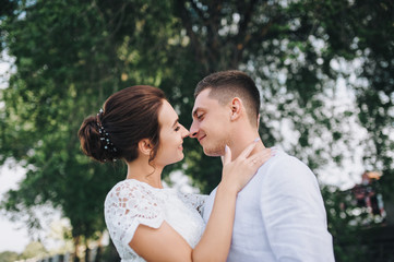 Fototapeta premium Beautiful newlyweds hugging against a background of green foliage. A stylish bridegroom gently presses a sweet bride. Wedding portrait close-up.