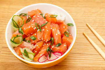Hawaiian poke with salmon and sesame seeds, boiled rice, fresh cucumber, radish and green onions in glass bowl