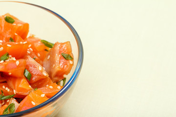 Hawaiian salmon poke with green onions and sesame seeds in glass bowl