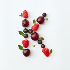 Summer pattern of letter K english alphabet from natural ripe berries - black currant, cherries, raspberry, mint leaf isolated on a white background.