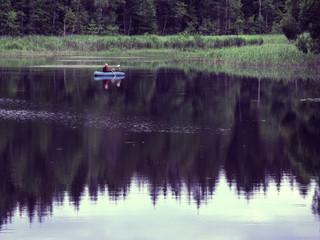 Two people on an inflatable boat in the distance enjoy a rest on the water. A beautiful place, a lake by the forest