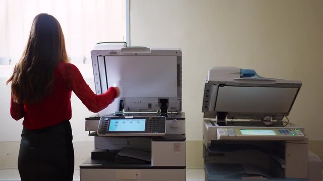 Beautiful secretary with photocopy machine and documents, girl working with photocopier at her job.