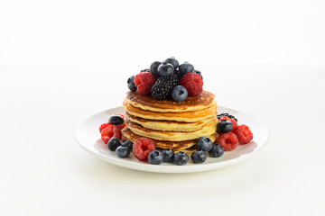 Stack of pancakes with fresh blueberry, raspberry and blackberry on white plate