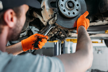 selective focus of professional worker repairing car without wheel in mechanic shop