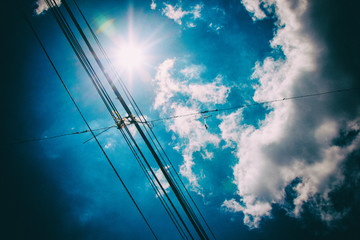 Electric and telecommunication wires with bright sun in a blue sky with clouds on the background....