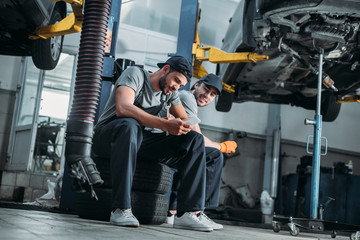 Fototapeta na wymiar two auto mechanics using smartphone and resting in auto repair shop
