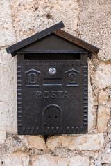 Vertical image of a mailbox with a wall in the background. No people.