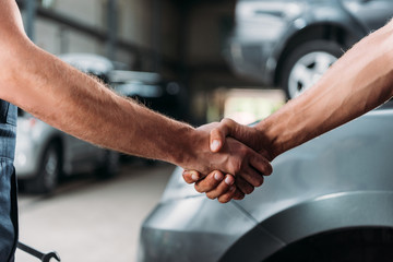cropped view of mechanics shaking hands in auto repair shop