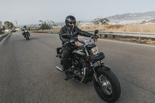 Man in black clothes riding a black classic American motorcycle in a road.