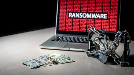 Hard disk file locked by chain and padlock with laptop computer monitor show red binary ransomware attacking, dollar banknote and key on the table. Cyber attack and internet data security concept