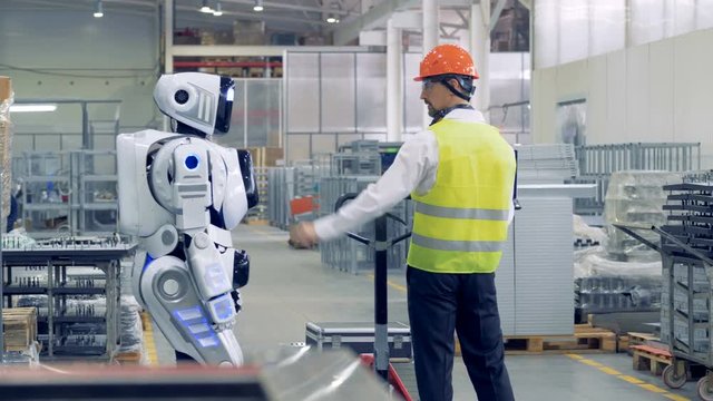 A man activates droid at a factory. A worker switches on a robot to make it pull a heavy cart with metal sheets.