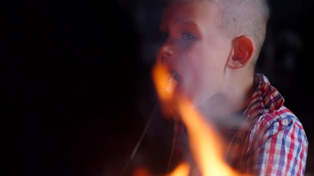 Cute boy eats marshmellow near the wood fire on picnic