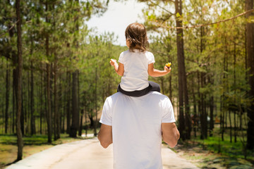 Father and child taking a walk together in a park outside. Green forest background.