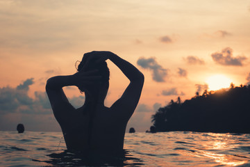 young woman from behind in indian ocean bathing and holding her hair during purple sunset with romantic mood