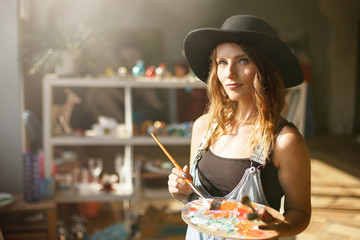 Portrait of handsome long-hair female artist in cute black hat mixed colors on the palette and...