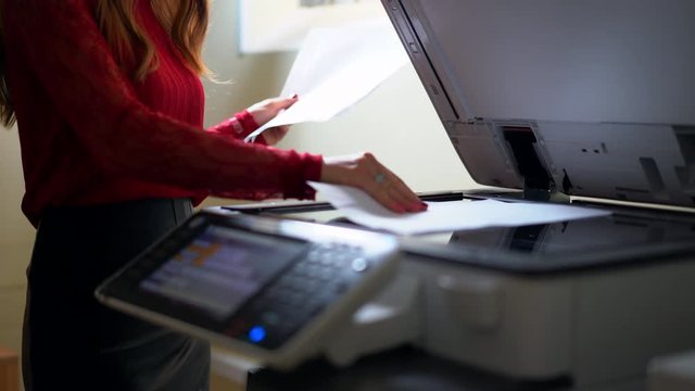 Young girl at office, pressing a button, turns on the printer and making copies of documents.