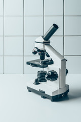 modern optical microscope on white tablet in front of tiled wall