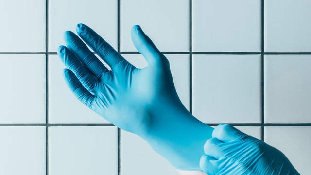 cropped shot of medical worker putting on blue rubber gloves in front of tiled white wall