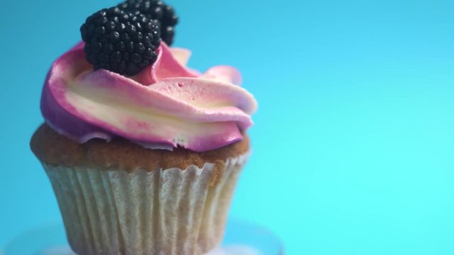A delicious and appetizing capkake with a pink filling rotates with two blackberries on a blue background.
