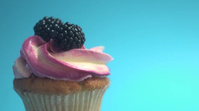 A delicious and appetizing capkake with a pink filling rotates with two blackberries on a blue background.