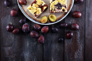 Rustic plum cake on wooden background with plums around.