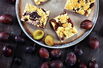 Rustic plum cake on wooden background with plums around.