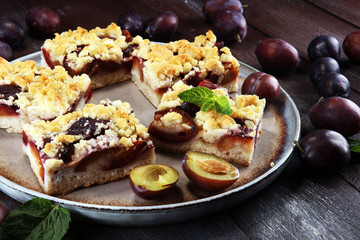 Rustic plum cake on wooden background with plums around.
