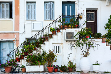 Fototapeta na wymiar Blue door and blue windows on a traditional Greek white facade with stairs and pots full of flowers in the afternoon