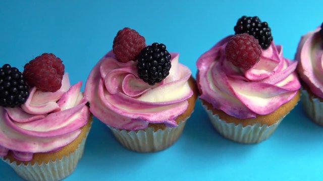 Delicious and appetizing capkake with a pink filling with two berries of blackberries and raspberries on a blue background. Four Cappey Cakes